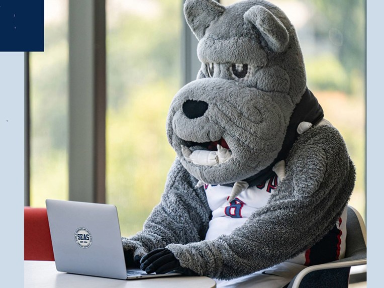 The costume mascot of Gonzaga university sits at a laptop computer